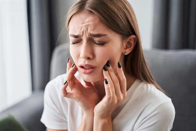 Woman experiencing severe tooth pain and sensitivity holding jaw with pained facial expression